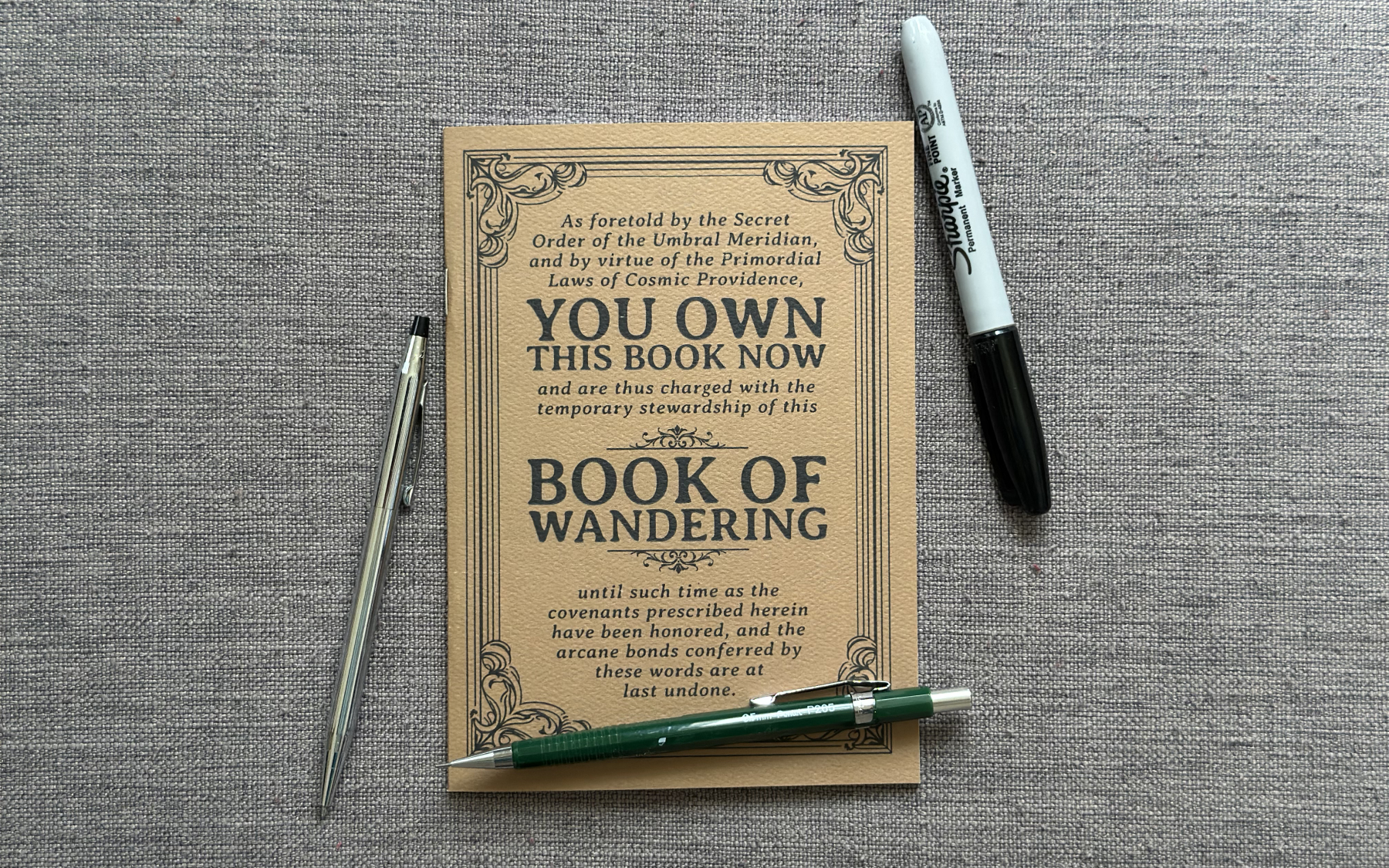 The Book of Wandering (a self-traveling journal) with a mechanical pencil, a pen and a Sharpie marker.